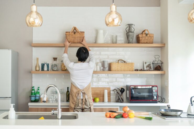 キッチン背面の見せる収納にバスケットを置くエプロン姿の男性