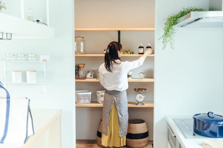 キッチン奥のパントリーに食材を片付けるエプロン姿の女性