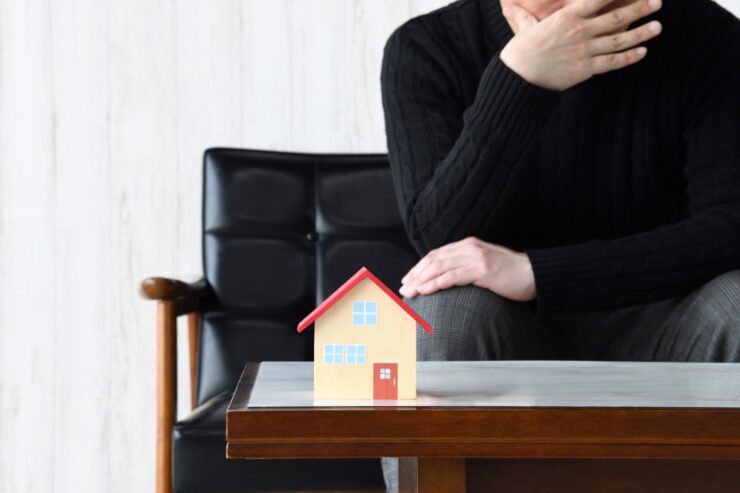 テーブルに置かれた住宅模型を前に、後悔している男性のイメージ