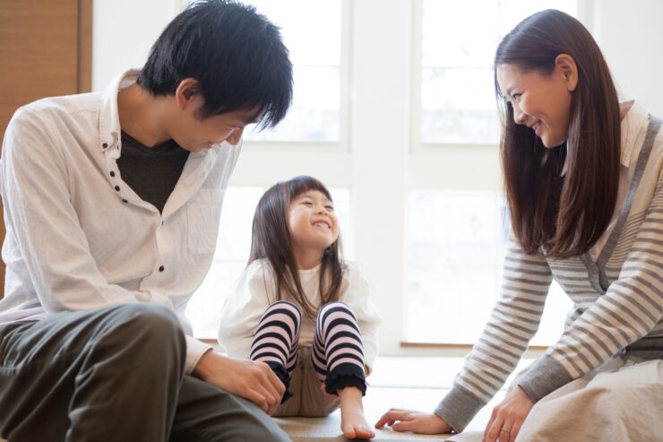 小上がり畳コーナーに腰をかけて笑い合う、夫婦と小さな女の子の3人家族