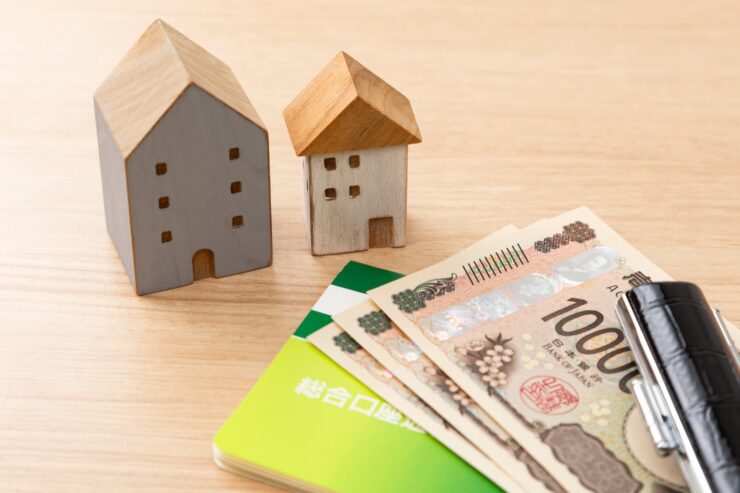 2つの家の模型、前に置かれた銀行通帳と1万円札、銀行印