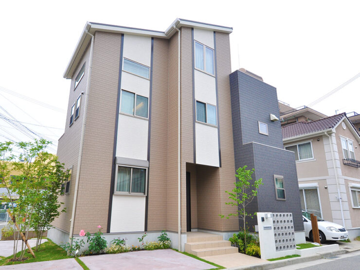 ライトブラウン、ベージュ、チャコールグレーの外壁を組み合わせた3階建ての住宅外観